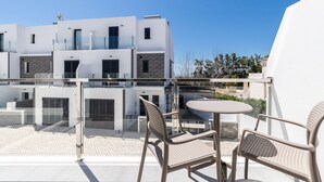 Un edificio moderno con balcón de vidrio, asientos exteriores y vistas despejadas del entorno.