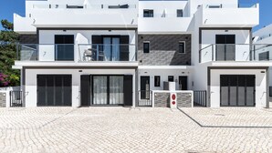Un edificio residencial moderno de varios pisos con un patio empedrado, balcones y puertas de garaje.