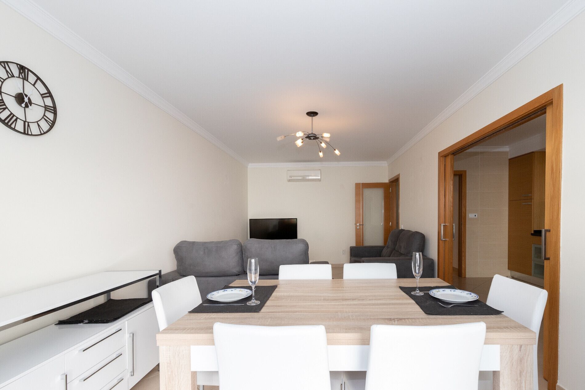A modern dining area with a wooden table, white chairs, and a clock on the wall.