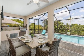 An outdoor patio with a pool, dining table, chairs, and a grill. - Heated Salt Water Pool, Kayaks, Villa Tropical Fruits - Roelens Vacations (Cape Coral)