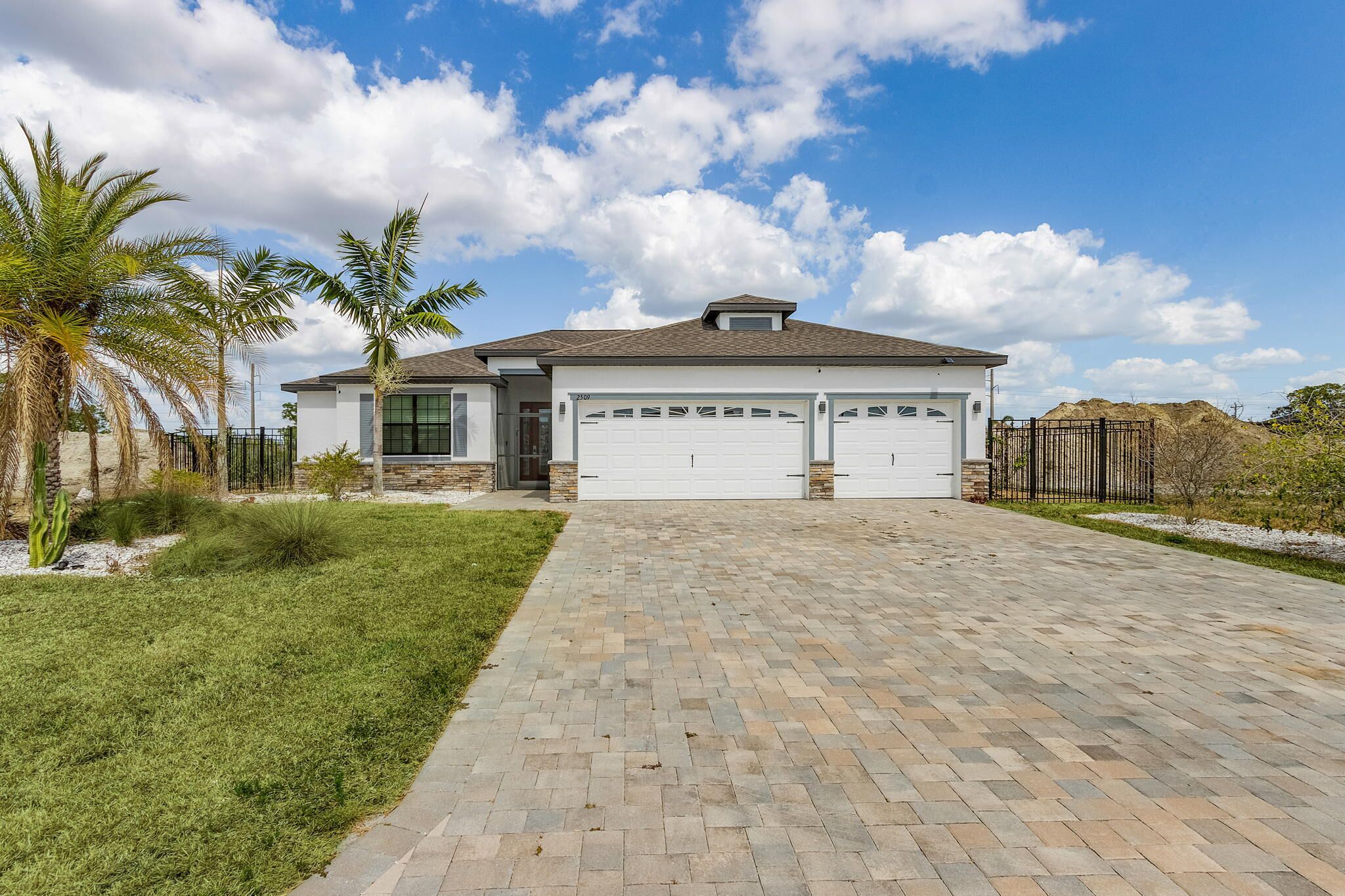 A modern two-story house with a paved driveway, garage, and landscaped yard with palm trees.