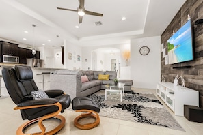 Una sala de estar moderna con un sofá modular, un sillón de cuero negro, una mesa de centro de vidrio y un televisor de pantalla plana grande montado en una pared de madera.
