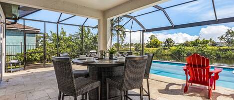 A covered outdoor patio with a pool, wicker chairs, and a red Adirondack chair.
