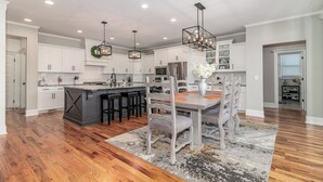 A spacious kitchen with white cabinets, a large island, and a dining area with a table and chairs. - Perfect Masters Rental in Golf Course Community - Bartram Trail CC: Augusta, GA  (Evans)