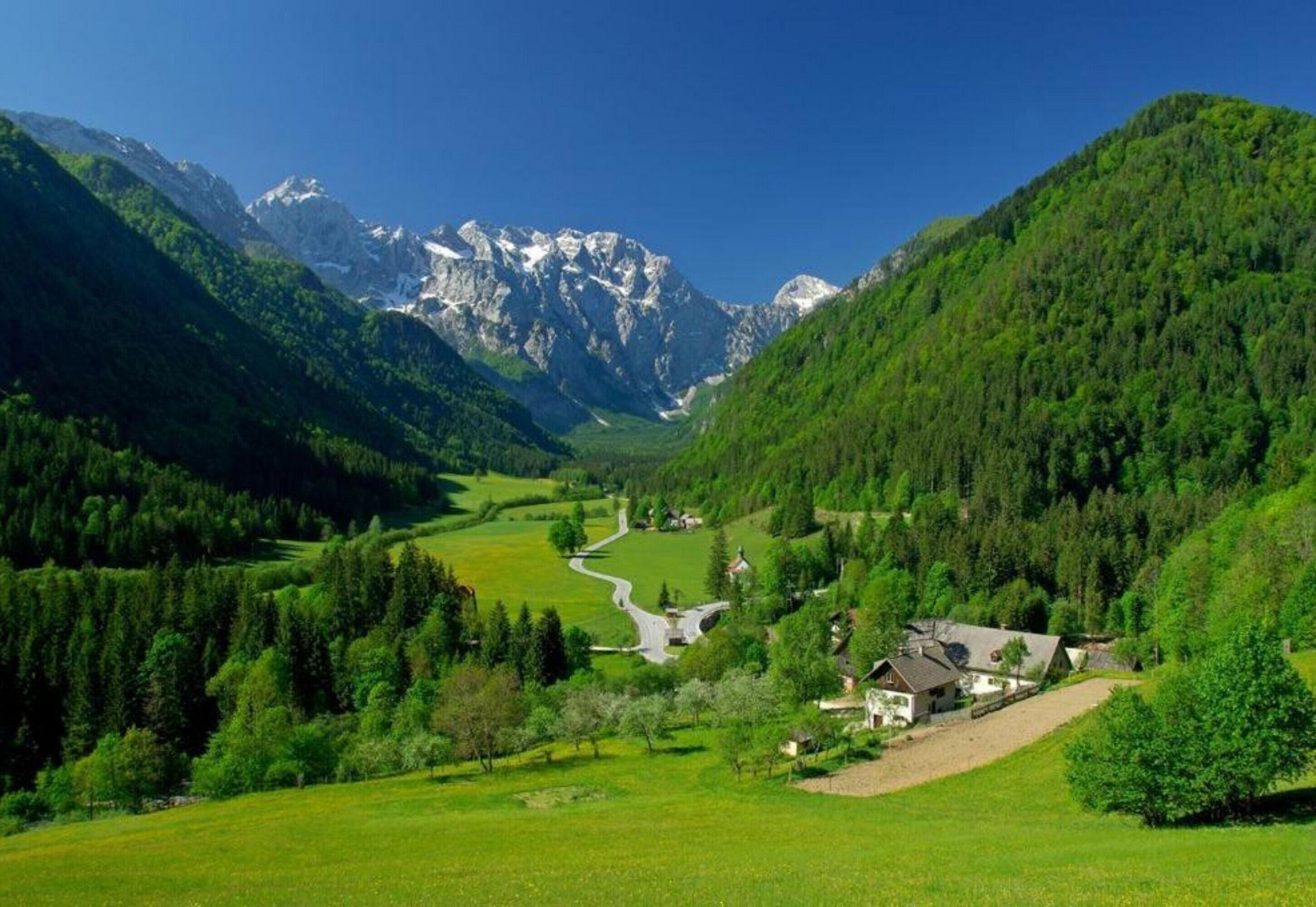 Paisagem montanhosa rural com uma pequena aldeia, casas e estrada sinuosa.