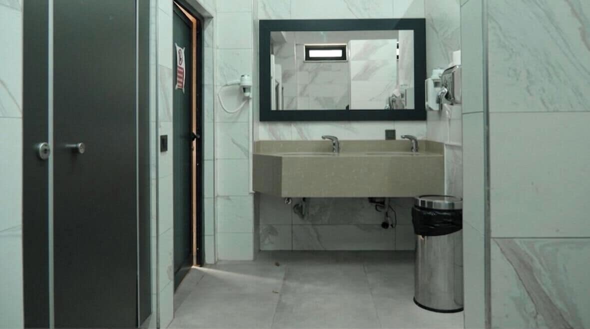 Un baño con lavamanos, espejo y cubo de basura.