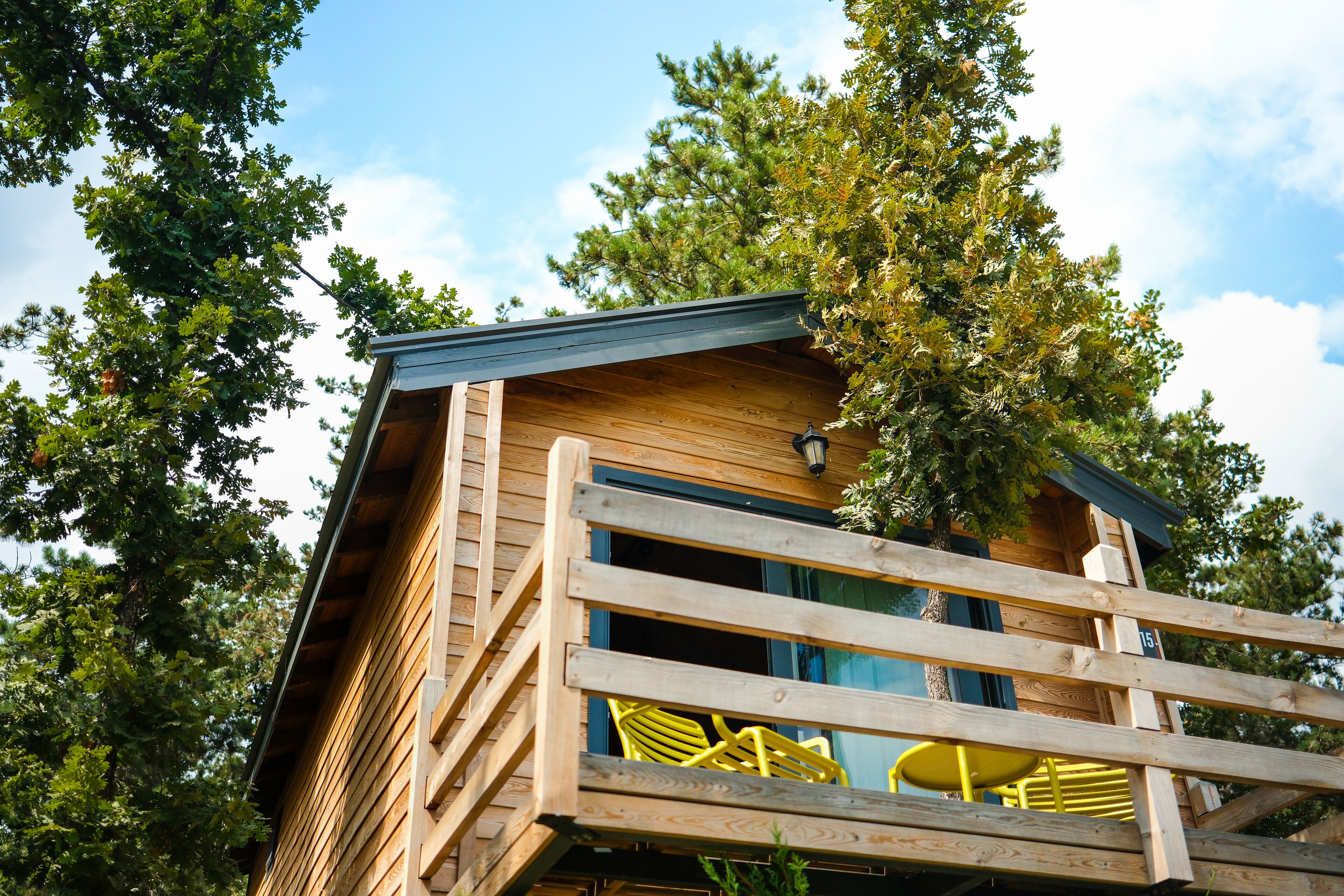 A wooden cabin with a balcony, surrounded by trees.