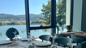 Ein Essbereich mit Blick auf einen See und Hügel, mit einem langen Holztisch, gedeckt für eine Mahlzeit.