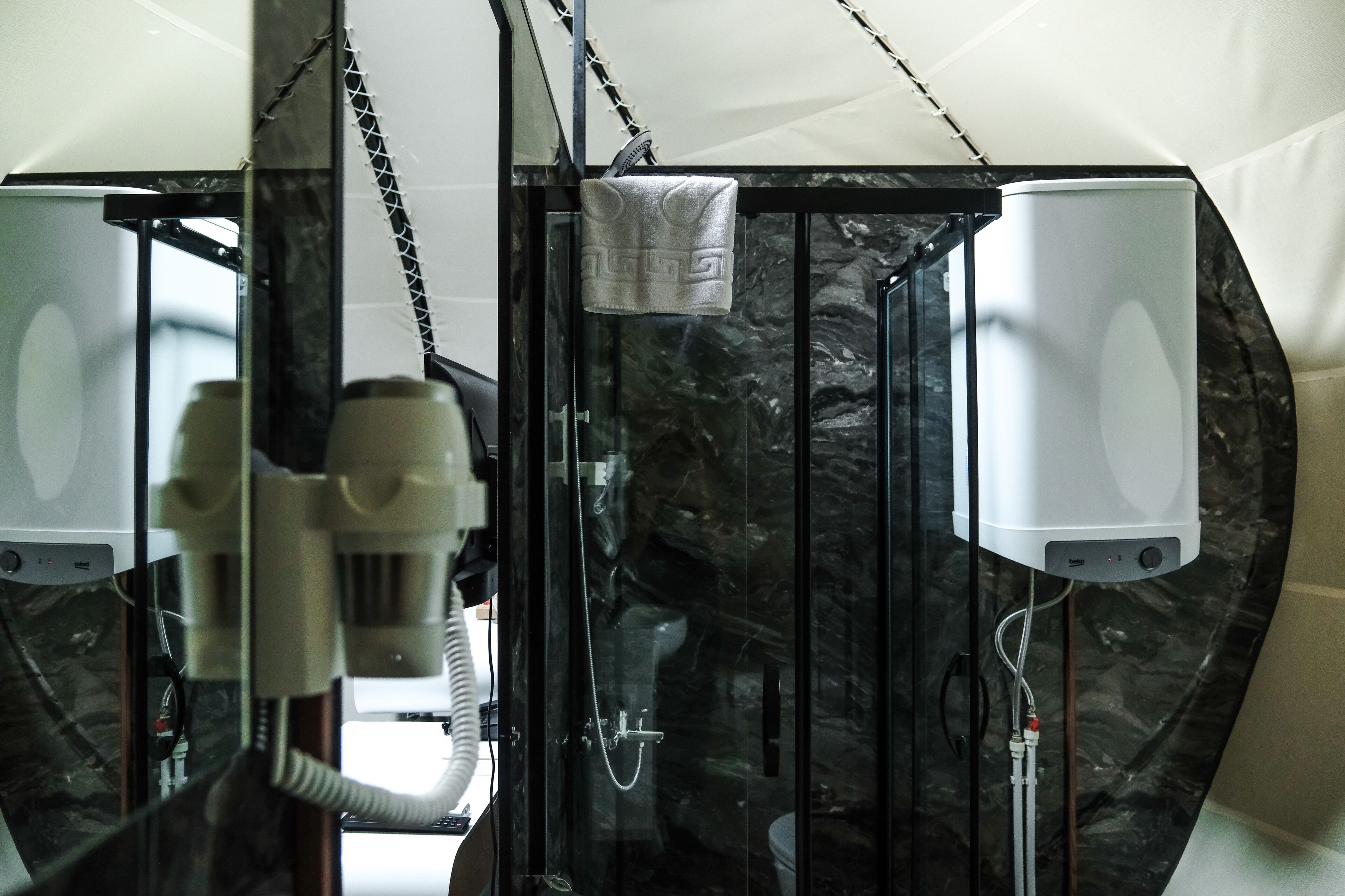 A bathroom with a glass shower enclosure, a towel hanging on a rack, and two white water heaters mounted on the wall.