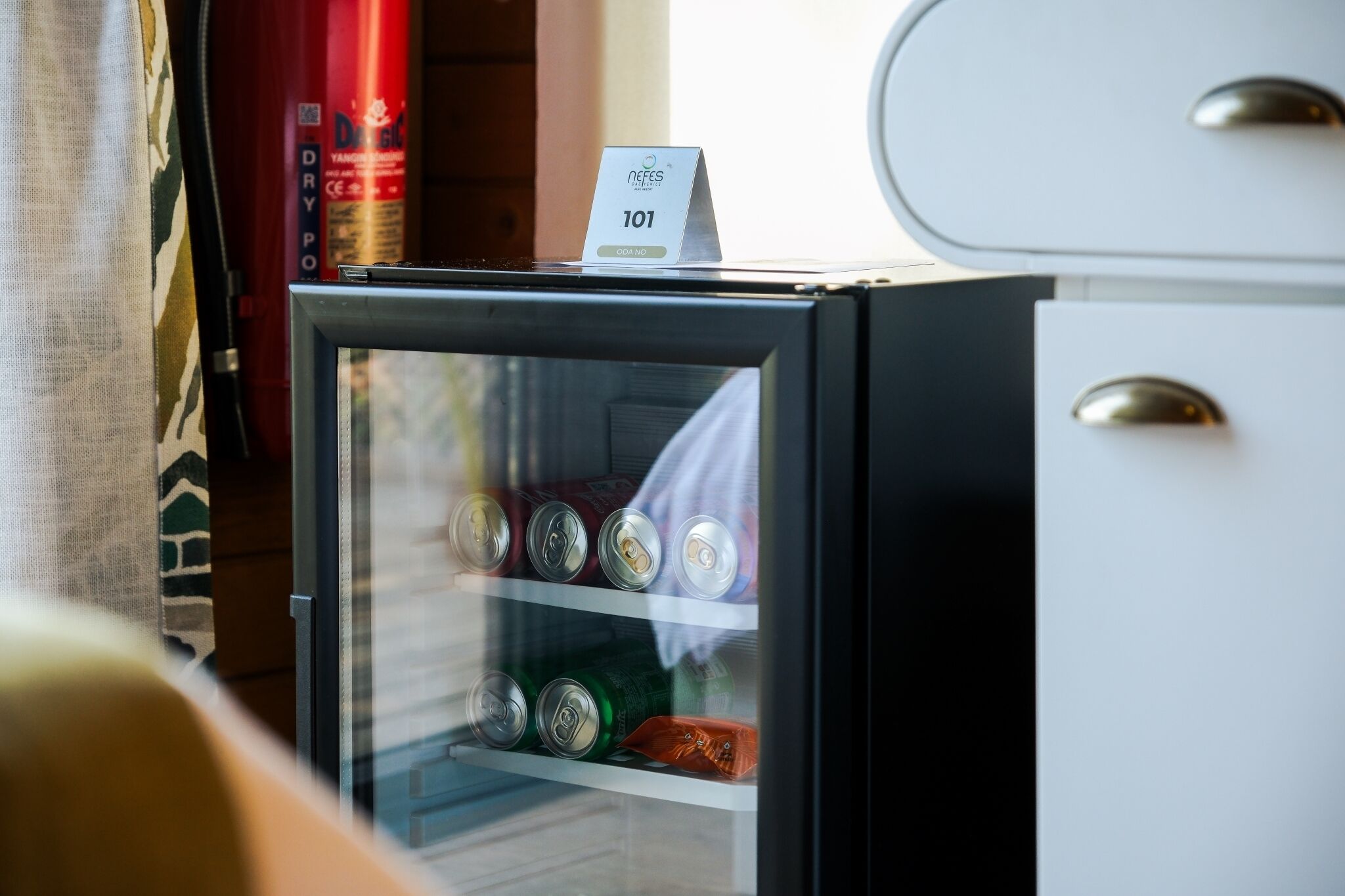 A minibar with a sign indicating room number 101, a fire extinguisher, and a window with a view.