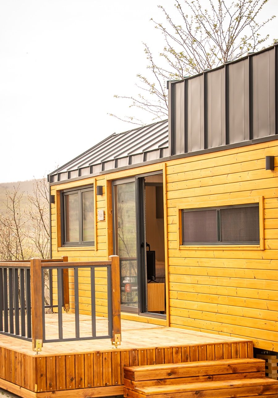 A modern wooden cabin with a deck, large windows, and a metal roof.