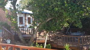 A wooden deck with outdoor seating, a small pool, and a building with a white facade and brick walls. - - Country getaway in Peaceful setting yet minutes from Town (Gqeberha)
