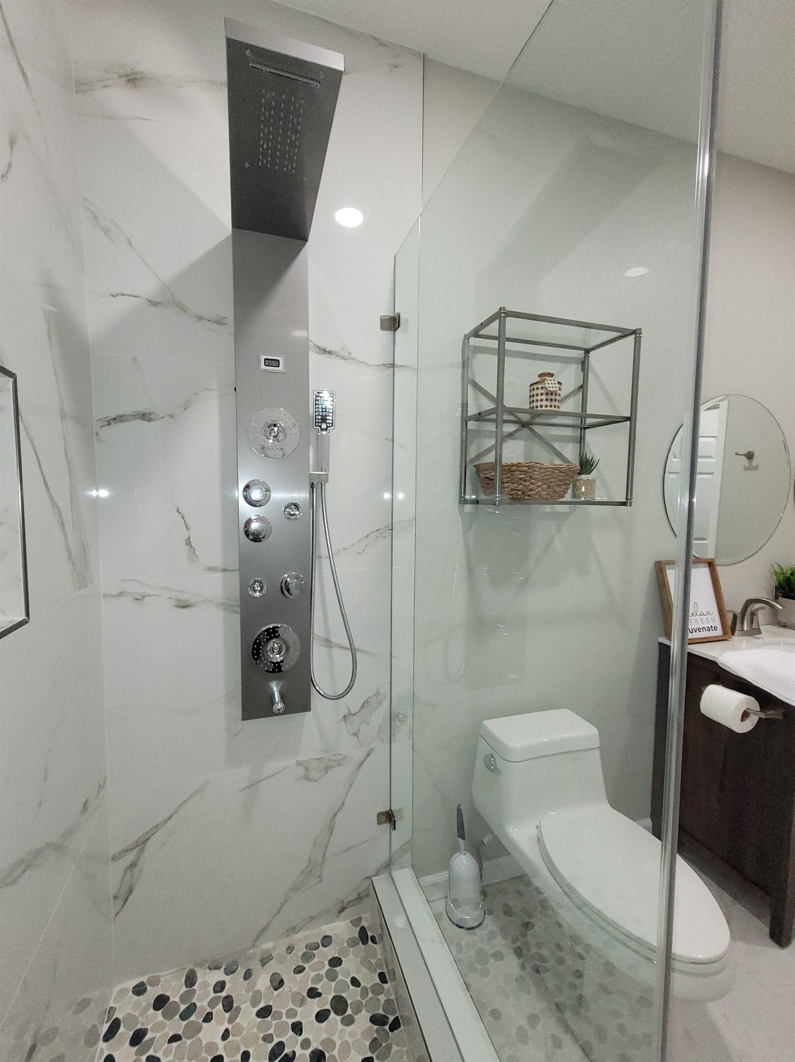 Un baño moderno con ducha envuelta en vidrio, inodoro y lavamanos con espejo.