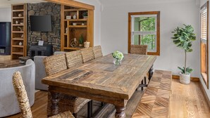 Ein Essbereich mit Holztisch, Korbstühlen, einer Steinwand und einem an der Wand montierten Fernseher.