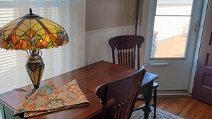 A dining area with a wooden table, chairs, a stained glass lamp, and a floral rug.