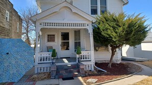 A two-story house with a front porch, a small garden, and a tree.