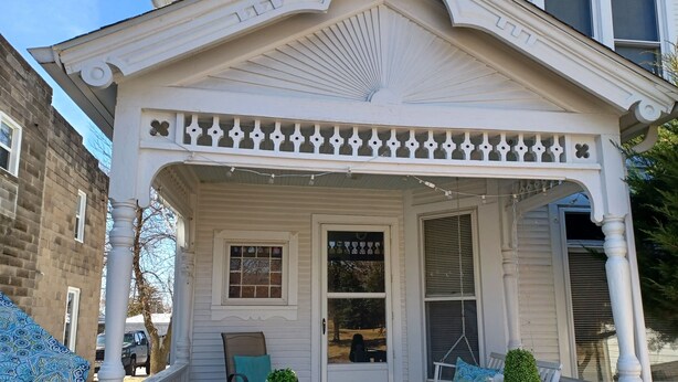 A white porch with a decorative balustrade, a bench with a cushion, and a small potted plant.