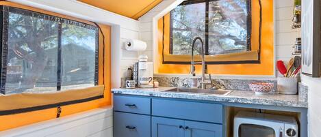 Una cocina compacta con ventana, un lavamanos, un microondas y un refrigerador pequeño.