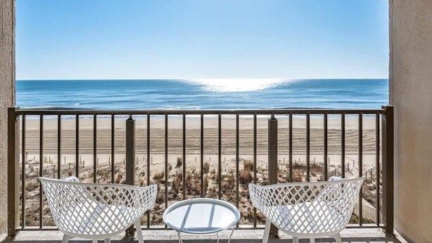 A balcony with a view of the beach, two white chairs, and a small table. - Three Bedroom Direct Oceanfront Condo with Pool (Ocean City)