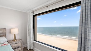 A bedroom with a large window, a bedside lamp, and a wooden nightstand. - Three Bedroom Direct Oceanfront Condo with Pool (Ocean City)