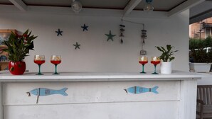 A white bar counter with decorative fish motifs, two potted plants, and two glasses of red drink. - Le Barchette 2 - Piano Terra (Lecce)