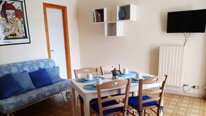 Un comedor con una mesa dispuesta para dos personas, un sofá y un televisor montado en la pared.