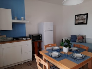 A compact kitchen with a microwave, toaster, and refrigerator. A dining table with blue placemats and plates is set for two. - Le Barchette 7 - Primo Piano (Lecce)