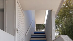 Una escalera con peldaños azules y beige que lleva a una puerta con celosía metálica.