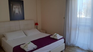 Habitación de hotel con cama, mesita de noche, lámpara roja, aire acondicionado y ventana con cortinas.
