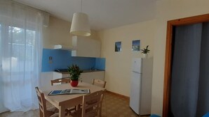 A compact kitchen with a dining table, chairs, a refrigerator, and a potted plant.