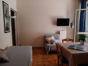 A room with a bed, a sofa, a table with a plant, and a TV mounted on the wall. - Le Barchette 5 - Piano Terra (Lecce)