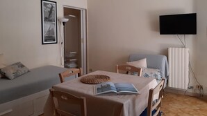 A room with a dining table, chairs, a sofa, a television mounted on the wall, and a radiator. - Le Barchette 5 - Piano Terra (Lecce)