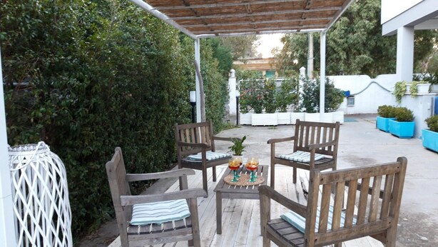 An outdoor patio with wooden chairs and a table, surrounded by greenery and white walls. - Le Barchette 5 - Piano Terra (Lecce)