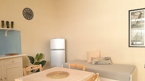 A small, well-lit room with a bed, a table with chairs, a refrigerator, a clock on the wall, and a framed picture. - Le Barchette 5 - Piano Terra (Lecce)