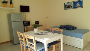 A compact living space with a kitchenette, a dining table with chairs, a sofa, and a TV mounted on the wall. - Le Barchette 11 - Primo Piano (Lecce)