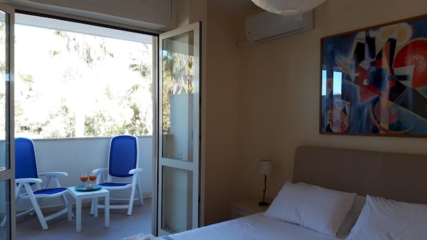A hotel room with a bed, a balcony with chairs and a table, and a painting on the wall. - Le Barchette 11 - Primo Piano (Lecce)