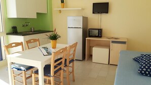 A compact living space with a kitchenette, a dining area with wooden chairs, a small TV, and a sofa with a patterned pillow. - Le Barchette 11 - Primo Piano (Lecce)