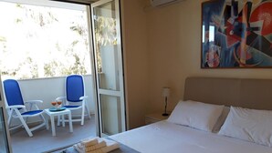 A hotel room with a bed, two chairs, a table with drinks, and a painting on the wall. - Le Barchette 11 - Primo Piano (Lecce)