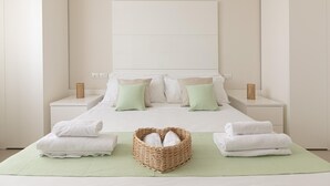 A neatly arranged hotel room with a large bed, two nightstands, a wicker basket with towels, and a green rug. - Residenza Excelsior 706 (Vasto)