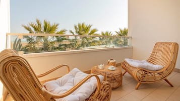 A balcony with wicker furniture, a table with a teapot and cup, and a view of palm trees.