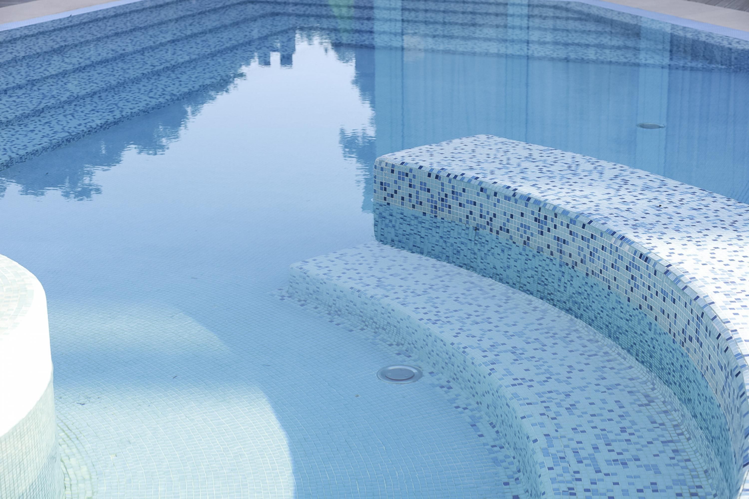 A clear blue swimming pool with a tiled edge and a drain in the center.