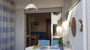 A dining area with a table set for two, a blue chair, a potted plant, and a hanging light fixture. - Le Barchette 12 - Primo Piano (Lecce)