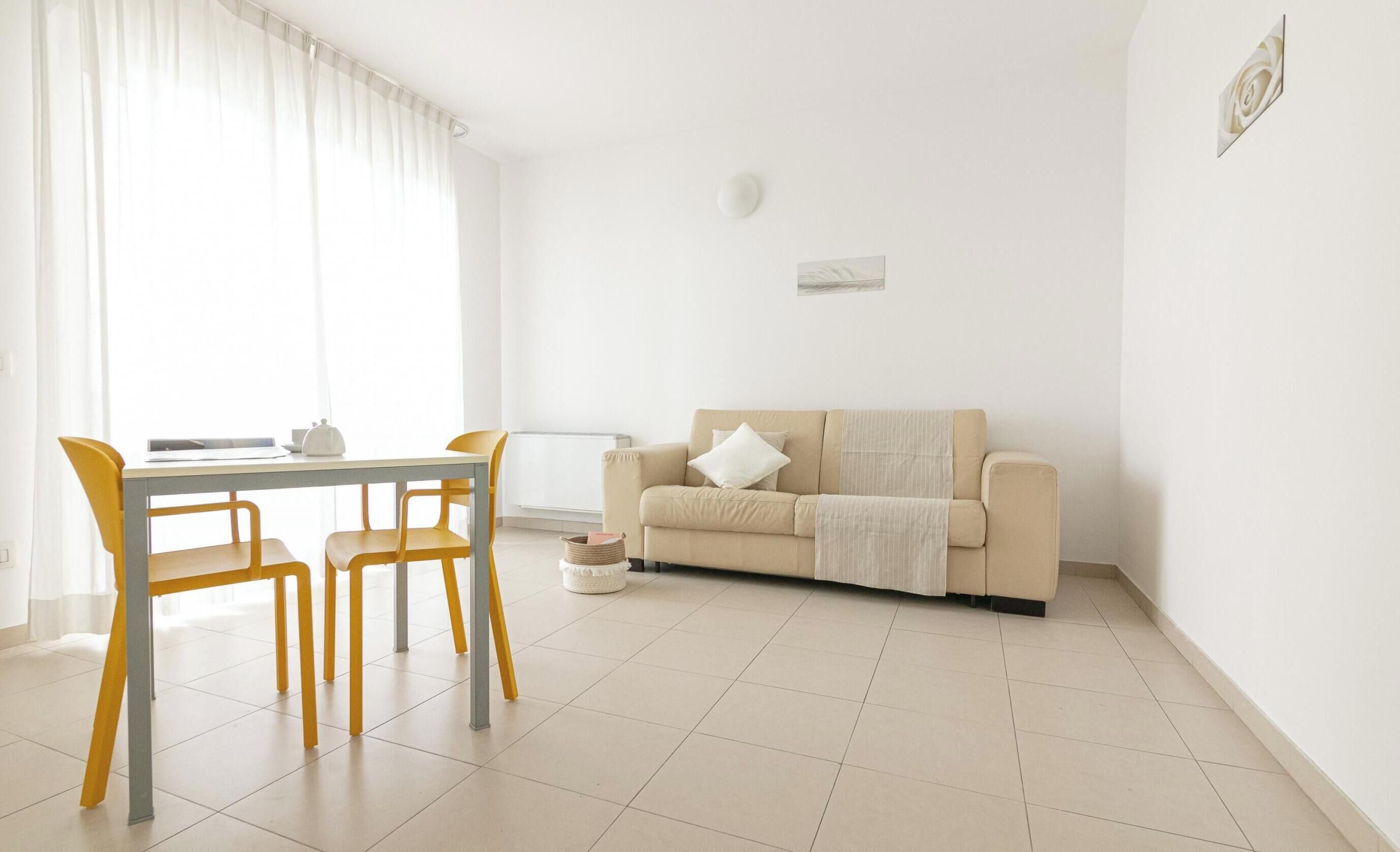A minimalist living room with a beige sofa, a dining table with yellow chairs, and a white curtain.