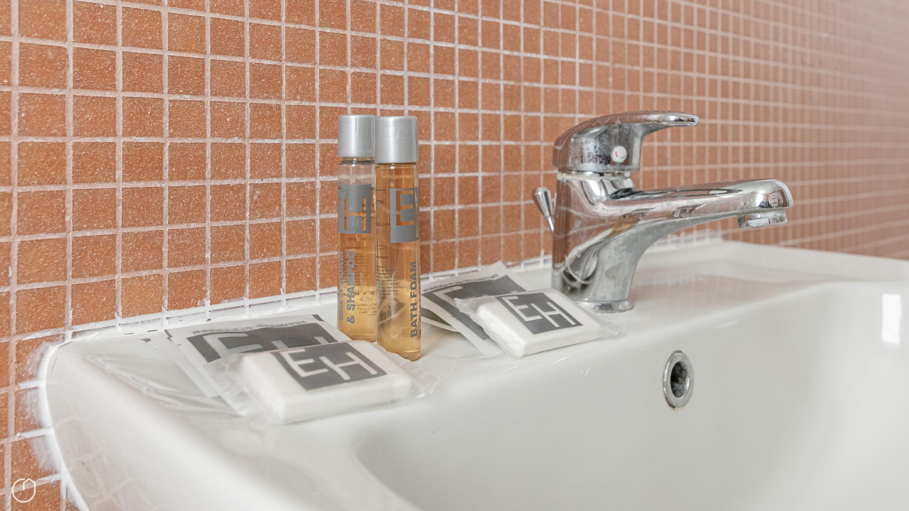 A bathroom sink with a chrome faucet, two bottles of bath foam, and a soap dispenser.