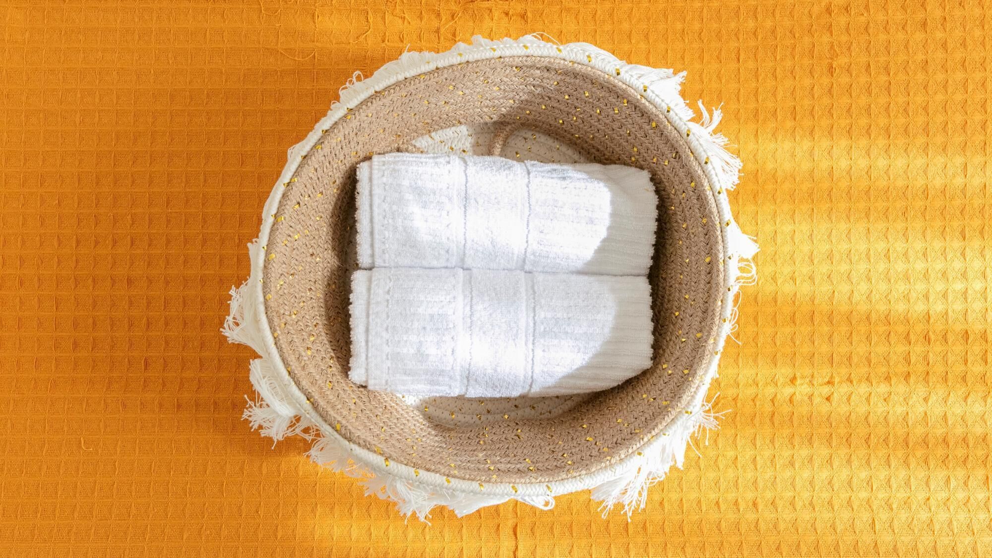 A cardboard box with a white towel inside, placed on a textured orange surface.