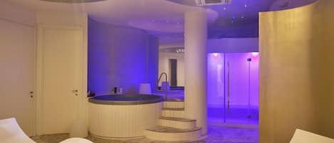 Een moderne spa ruimte met een jacuzzi, witte lounge stoelen en een trap naar een douchegedeelte.