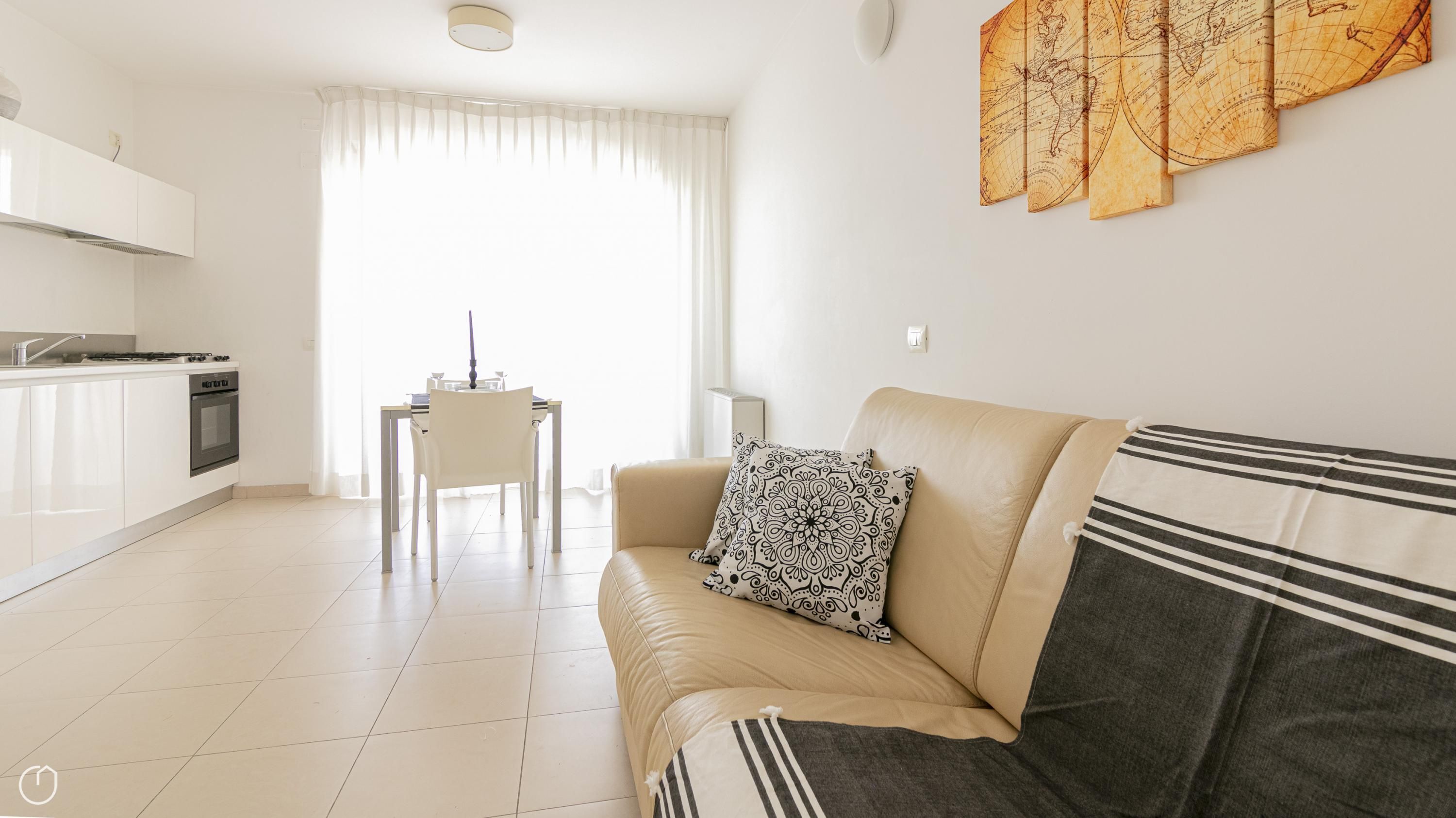 A modern living room with a sofa, a dining table, and a kitchen area with white cabinets and a stove.