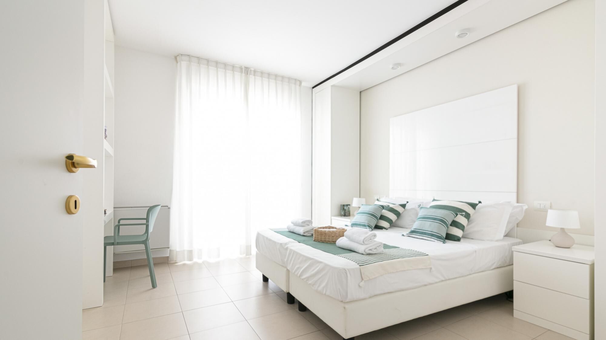 Ein modernes Schlafzimmer mit einem großen Bett, einem Nachttisch, einem Sessel und einem Fenster mit Vorhängen.