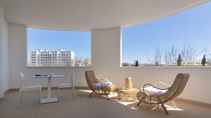 Un balcón con una mesa y sillas, una silla de mimbre y una pequeña mesa redonda con cojín.