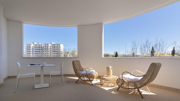 Un balcone con un tavolo e sedie, una sedia in vimini e un tavolino rotondo con un cuscino.